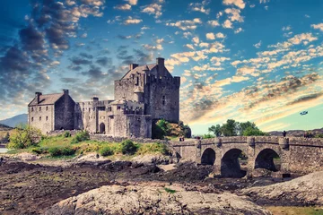Poster Medieval Eilean Donan Castle in Scotland.  Old fairytale castle near lake in beautiful golden evening light. Medieval castle landscape with sunset in background. © N