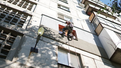 Insulation of the walls of the house. Worker hanging on the ropes