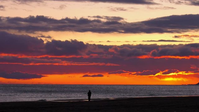 Dramatic beach sunrise with older man silhouetted against silver sea at dawn