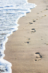 Foot prints at beach sand. White bright wave, sea foam.