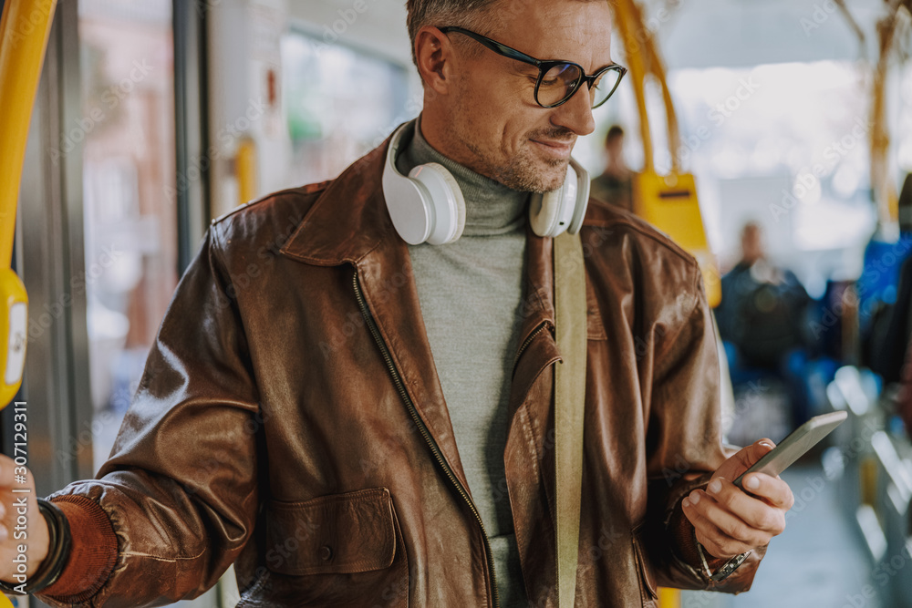 Wall mural attractive smiling man using smartphone in tram