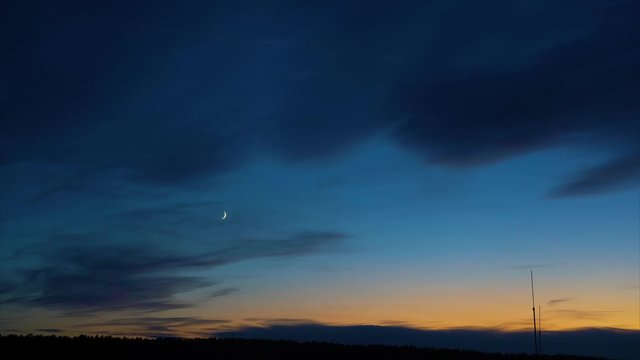 Twilight sky after sunset. Young month against the blue sky. The smooth movement of the clouds. Time lapse.