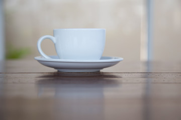 A white cup of coffee placed on a wooden table by the window in a coffee shop, Concept: Delicious breakfast drinks fragrant suitable for lifestyle, closeup cup of coffee over the top with space