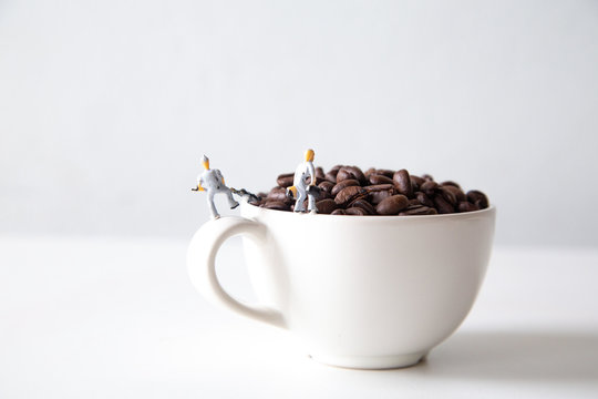 miniature people standing on a white coffee cup with brown coffee beans, Concept: teamwork professionalism and beverage business ideas successful, close-up macro toy small creative lifestyle - Powered by Adobe
