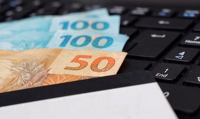 Credit card and Brazilian money on laptop keyboard. Online shopping concept. Real banknotes.
