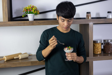 An Asian handsome guy is happy to eat fruit yogurt