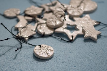 Small ornament pendant star shape, snowflake round figures from white clay and shining glitter. Shallow depth of focus, bokeh effect on blue background. Christmas and New year decoration, jewel gift.