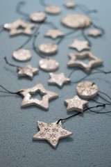 Small ornament pendant star shape, snowflake round figures from white clay and shining glitter. Shallow depth of focus, bokeh effect on blue background. Christmas and New year decoration, jewel gift.