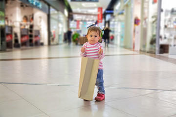 Black friday concept, shopping with children, nature of friendly shopping. little cute baby girl holds craft paper bag for shopping and smiles slyly. close-up, soft focus, in the background shops