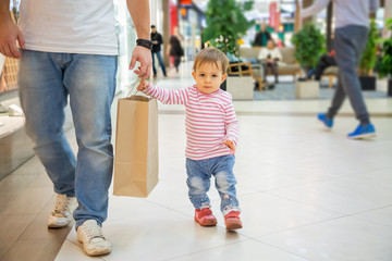 Black friday concept, shopping with children. little cute girl with dad holds a craft paper bag for shopping and looks at the camera. close-up, soft focus, in the background a shopping center in blur