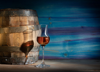 Glass with strong alcohol on a blue wooden background with an oak barrel