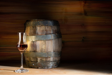Glass with strong alcohol on a wooden background with an oak barrel