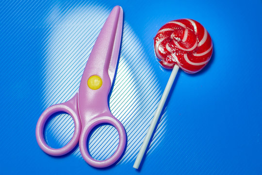 pink cissors and Lollipop on blue blue background and ribbon