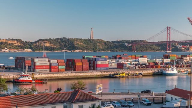 Skyline over Lisbon commercial port timelapse, 25th April Bridge, containers on pier with freight cranes, city train Lisbon, Portugal. Aerial view before sunset