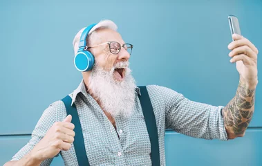 Foto op Plexiglas Happy senior man taking selfie while listening music with headphones - Hipster mature male having fun using mobile smartphone playlist apps - technology and elderly lifestyle people concept © Alessandro Biascioli