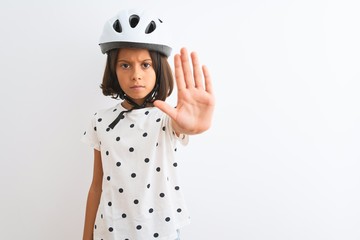 Beautiful child girl wearing security bike helmet standing over isolated white background doing stop sing with palm of the hand. Warning expression with negative and serious gesture on the face.