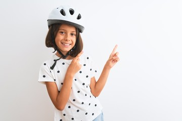 Beautiful child girl wearing security bike helmet standing over isolated white background smiling and looking at the camera pointing with two hands and fingers to the side.