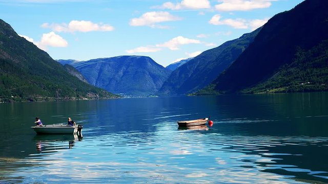 Beautiful Norwegian Travel Footage of the Lustrafjord with calm water and reflections of mountain forest, and two small boats, one moored and one moving slowly to the left.