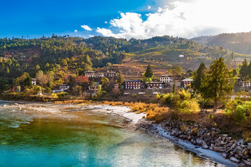 Mo Chhu River on a nice sunny day, Punakha, Bhutan. View from the wooden cantilever bridge near Punakha Dzong to river, houses of Punakha city and Himalaya mountains covered with forest. - obrazy, fototapety, plakaty