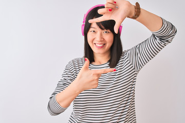 Obraz na płótnie Canvas Chinese woman listening to music using pink headphones over isolated white background smiling making frame with hands and fingers with happy face. Creativity and photography concept.