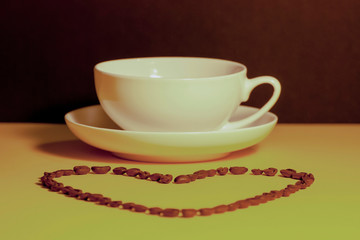Heart shape made from coffee beans in front of a coffee cup