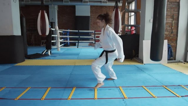 Wide shot of Caucasian female kickboxer wearing white kimono training indoors using special equipment