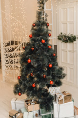 Christmas artificial tree with red balls and decor on it. Christmas and New Year's gifts under the Christmas tree in a bright interior