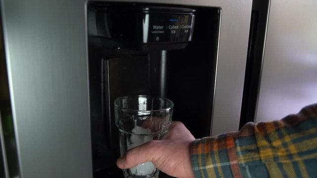 Ice falling to a glass from the ice maker on the fridge, slow motion