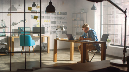 Professional Creative Designer Works on a Laptop in Loft Office, Drawng Product Sketches and Concepts. Stylish Design or Gaming Content Development Studio. Shot with Sunlight Flare.