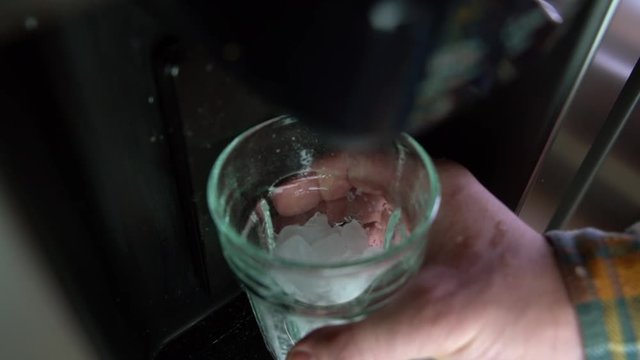 Ice falling to a glass from the ice maker on the fridge, slow motion