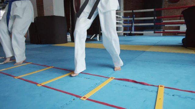 Young barefoot female karatekas wearing white kimono practicing indoors using special equipment