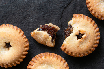 Broken open traditional british christmas mince pie with fruit filling next to whole mince pies on black slate. Top view. Copy space. © Moving Moment