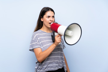 Young brunette woman over isolated blue background shouting through a megaphone