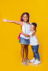 Little black siblings posing together on yellow background in studio