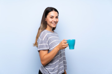 Young brunette woman over isolated blue background holding hot cup of coffee