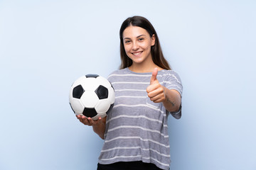 Young brunette woman over isolated blue background holding a soccer ball