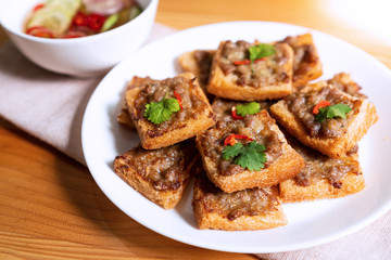 Close up of fried bread with minced pork spread in white plate on wood table.