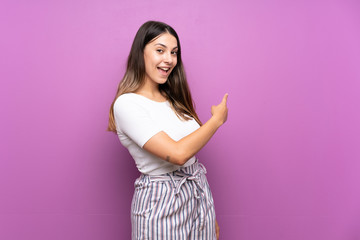 Young woman over isolated purple background pointing back