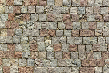 An old damaged stoneblock pavement cobbled with square stone blocks of different colors