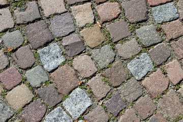 An old stoneblock pavement cobbled with square stone blocks with grass between blocks