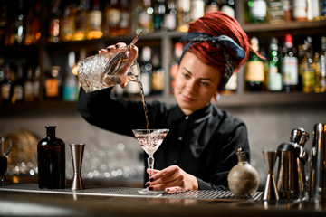 Bartender pours drink using glass with strainer inside