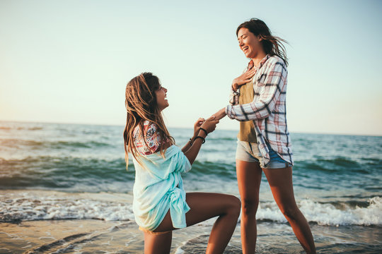 Woman proposing to her happy girlfriend on the beach