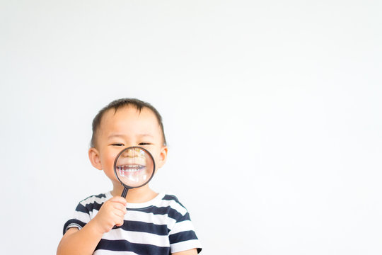 Little toddler boy child holding magnifying glass and showing front teeth with big smile on green grass: Healthy happy funny smiling face young adorable lovely boy kid with new tooth dental.