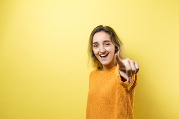 Happy young caucasian female in an orange sweater pointing fingers away..