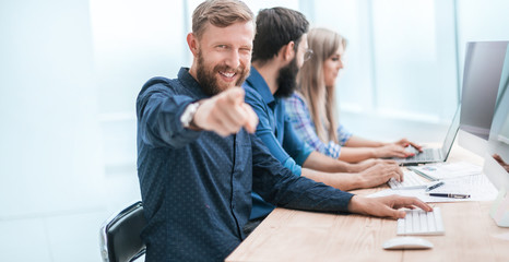 cheerful employee sitting at the office Desk and pointing at you.