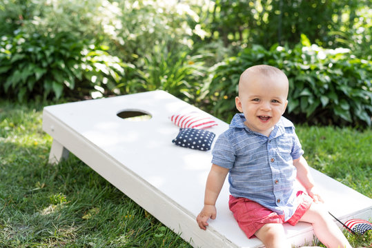 Kid Sitting On Cornhole Board In Backyard On Fourth Of July