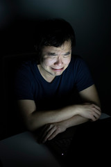 man freelancer or gamer with sad crying face with laptop in night in darkness in home