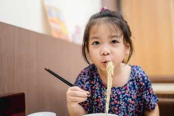 5 years old asian little girl eating and trying to use chopsticks.She hungry and delicious moment action with egg noodles soup in chinese restaurant in Hong kong.