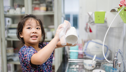 Happy smiley laughing face little cute asian girl washing dishes in kitchen for help her mom.Child...