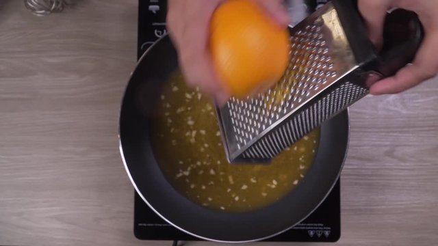 Close up on female hands grating orange zest into frying pan